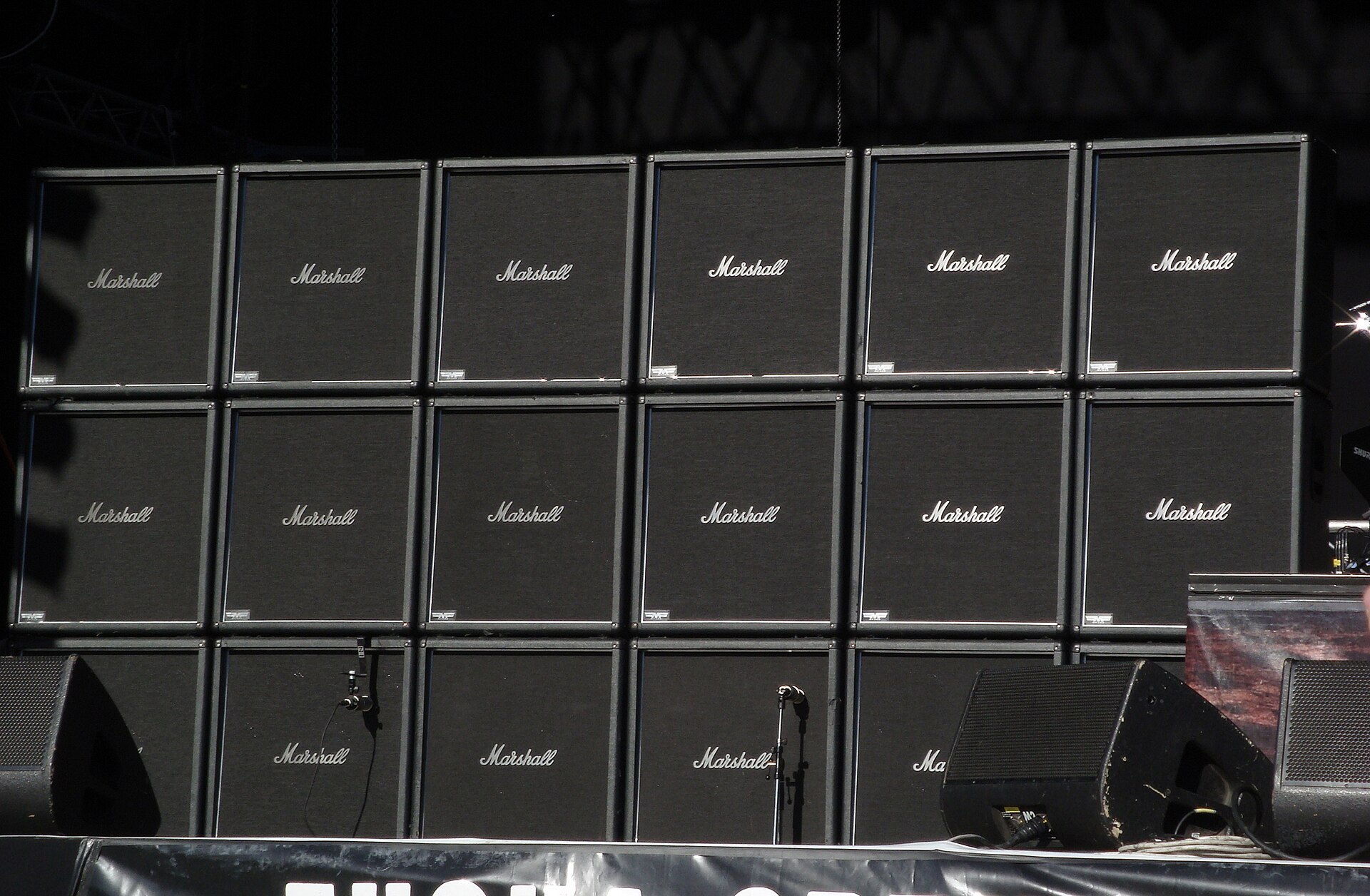 A wall of stacked amplifier and loudspeaker cabinets behind a stage with floor monitors